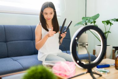 Güzellik videolarımı takip etmeyi unutma. Çocuk moda blogcusu ütüyle saçını düzeltiyor ve sosyal medya kanalı için bir video kaydediyor. 