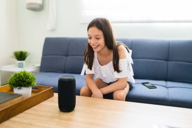 Neşeli çocuk akıllı hoparlörünü evde kontrol ediyor. Oturma odasında komut verip müzik çalan tatlı bir kız.