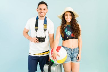 Neşeli turistler tatilleri sırasında tropikal bir yeri keşfetmeye hazırlar. Kamera ve plaj topu taşıyan genç bir çift.