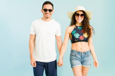 Erkek arkadaş ve kız arkadaş sahilde yürürken el ele tutuşuyorlar. Mayolu güzel bir çiftin, mavi arka planda poz verirken çekilmiş bir fotoğrafı.