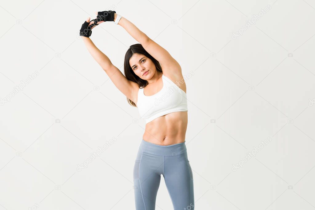 Dedication is key to have a fitness lifestyle. Portrait of an active woman in sportswear stretching up her arms and warming up while making eye contact