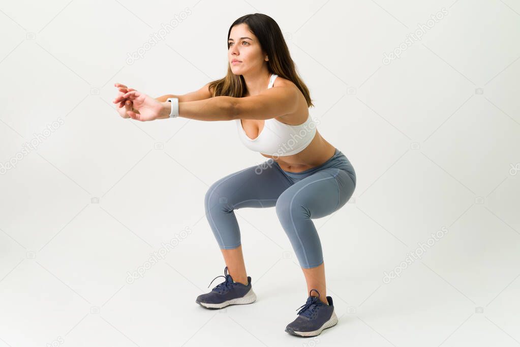 Squats are the best exercise for your legs. Fitness slim woman in activewear doing a squat workout against a white background 