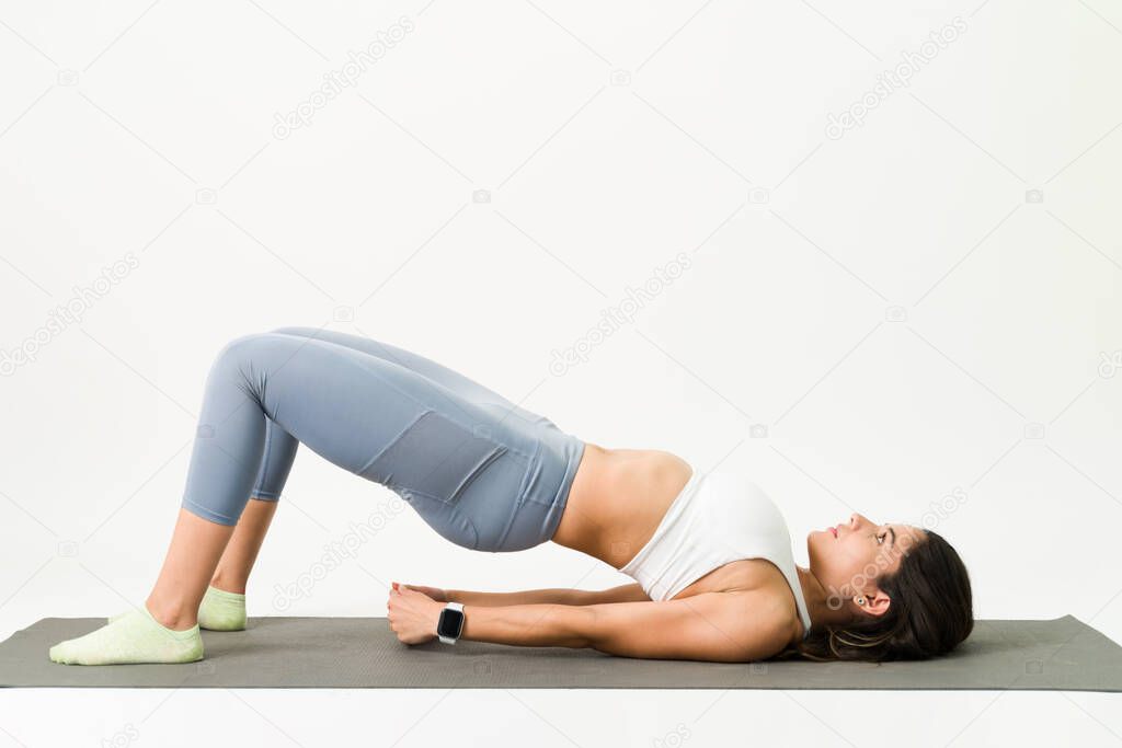 Focused young woman maintaining a bridge pose. Active woman exercising her buttocks and back muscles with a yoga workout