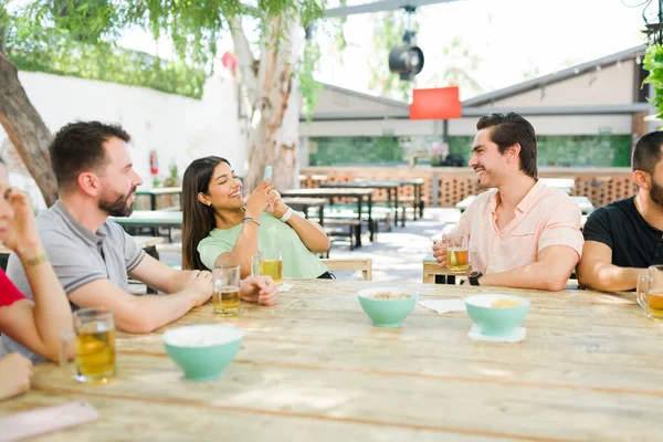 Sharing happy moments on social media. Attractive young woman taking a picture of her friends while enjoying drinks together at an outdoor bar