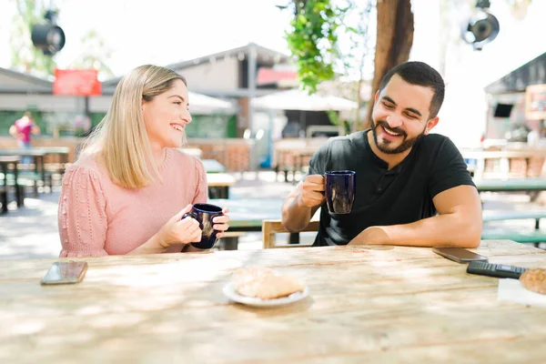 午後のコーヒーデートでは リラックスした白人女性とラテン人の男性が笑いながら一緒に冗談を言いました 屋外でブランチを楽しんでいる親友 — ストック写真