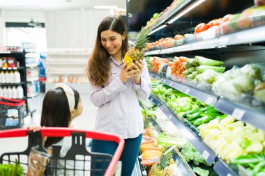 Lezzetli ananas. Mutlu, çekici bir anne, süpermarkette sağlıklı bir akşam yemeği alırken küçük çocuklarıyla gülümsüyor ve konuşuyor.