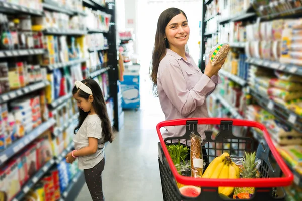 一个迷人的年轻女子和她的小孩在超市过道上选择商品时 笑着和眼神交流的画像 — 图库照片