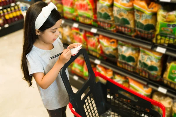 スーパーでショッピングカートを押しながら 買い物リストとメモを見てかわいい小学生 食料品店の愛らしい子供 — ストック写真