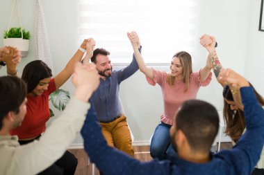 Attractive young people at an alcoholic anonymous group holding hands and celebrating their successful meeting session clipart