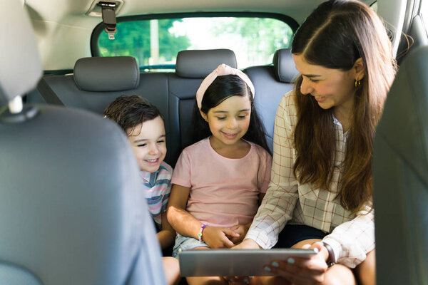 Do you like this movie? Happy young mom putting a movie or video on a tablet for her kids to watch during a quick trip on the car