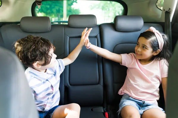 Give me a high five! Beautiful little boy and elementary latin girl having fun and doing a high five while sitting inside the car