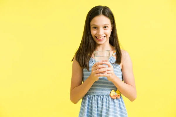 一个迷人的小女孩的画像 她穿着一件可爱的衣服 手里拿着一杯水 口渴的孩子笑着在黄色的背景下喝水 — 图库照片