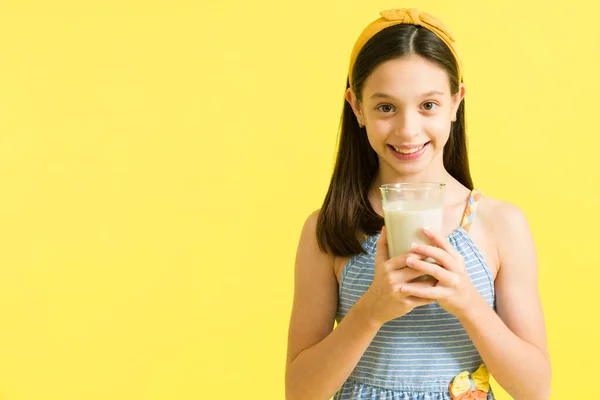 ミルクが好き 美しい若い女の子おいしいミルクと笑顔のガラスを保持します 明るい黄色の背景に対して牛乳を飲む髪の弓でPreteen — ストック写真