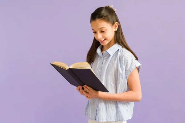 かわいい女の子が本で面白い話を読んでいます スマートPreteen女の子楽しみますA小説に対して紫色の背景 — ストック写真