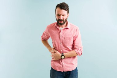 Safra taşı yüzünden acı çeken hasta bir adam. Safra kesesi hastalığı olan Latin bir genç adam karnının bir tarafına dokunuyor.