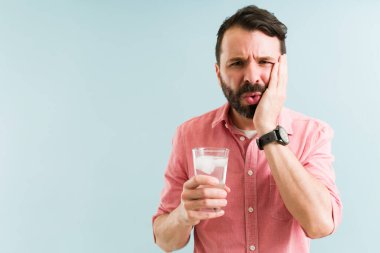 30 'lu yaşlarındaki üzgün Latin bir adam bir bardak soğuk su içtikten sonra yüzünü ovuyor ve diş hassasiyetinden muzdarip oluyor. 