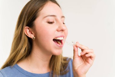 Sağlıklı beyaz dişlerini düzeltmek için ağzına görünmez diş düzenleyicileri koyan mutlu bir kadın.