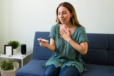 Çok heyecanlı ve neşeli hissediyorum. 20 'li yaşlardaki mutlu genç bir kadın pozitif hamilelik testini evinde tutuyor.