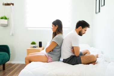 Angry couple in sleepwear ignoring each other in the bedroom. Upset girlfriend and boyfriend not talking because of a big fight
