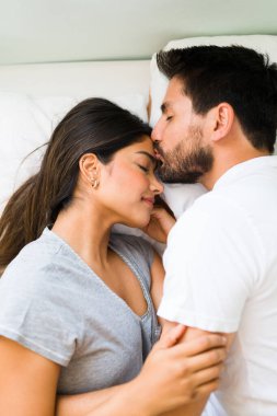 You are my everything. Young man in love giving a tender kiss to his girlfriend on the forehead while lying in a comfy bed 