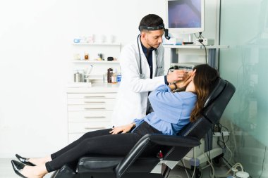 Kulak enfeksiyonum var. Latin otolargolog ofisinde bir kadın hastanın kulağına tıbbi teşhis koymaya çalışıyor. 