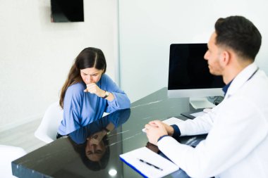 Hasta genç bir kadın öksürüyor ve bir doktorla belirtileri hakkında konuşuyor. Solunum sorunları olan kadın hasta kötü bir soğuk algınlığından muzdarip.