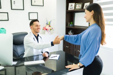 Gülümseyen İspanyol doktor ve cerrah sırasının arkasında oturan gülümseyen bir hastayı selamlıyor.