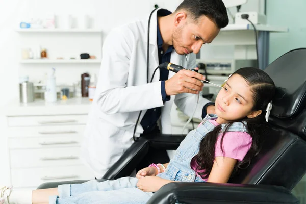 Ill little girl visiting a pediatrician due to an ear infection. Male otolaryngologist checking the ear of a small kid with hearing problems