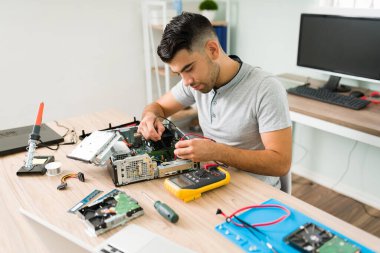 Bilgisayar çalışıyor mu? İspanyol adam tamir atölyesindeki bilgisayar bağlantılarını kontrol ediyor. Bozuk bir işlemcinin voltajını ölçmek için çoklu metre kullanan teknisyen