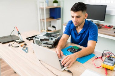Latin teknisyen bir işlemciyi laptopa bağlıyor ve bir müşteri için veri yedeği üzerinde çalışırken bilgisayarda yazıyor.  