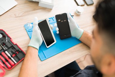 Bir erkek teknisyenin tamirhanesinde cep telefonunu parçalarken görüntüsü. Genç adam bozuk bir akıllı telefonun pilini değiştiriyor.