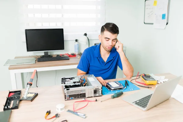 How can I help you? Young man talking on the phone and offering tech support to a customer. Technician trying to find a replacement part to repair a computer