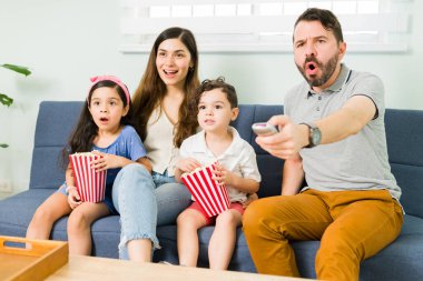 Ne büyük şok. İspanyol anne, baba ve küçük çocuklar TV 'de aile filmi izliyorlar ve patlamış mısır ve atıştırmalık yerken şaşırmış görünüyorlar.