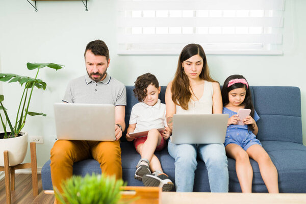 Beautiful family of four sitting together on the couch and typing on the laptop. Mom, dad and kids entertaining themselves on a leisure day 