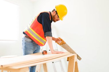 Yeni bir duvar inşa etmeden önce tahta bir çubuk kesmek için testereyle testere kullanırken odaklanmış bir marangozun yan görüntüsü