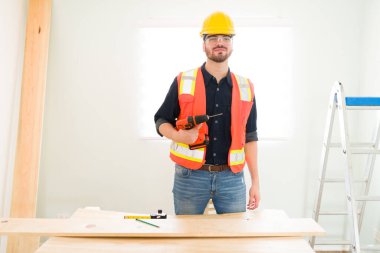 Elinde elektrikli matkap tutan profesyonel bir müteahhit portresi ve yeni bir ev inşa etmek için biraz odun kesmeye hazır.