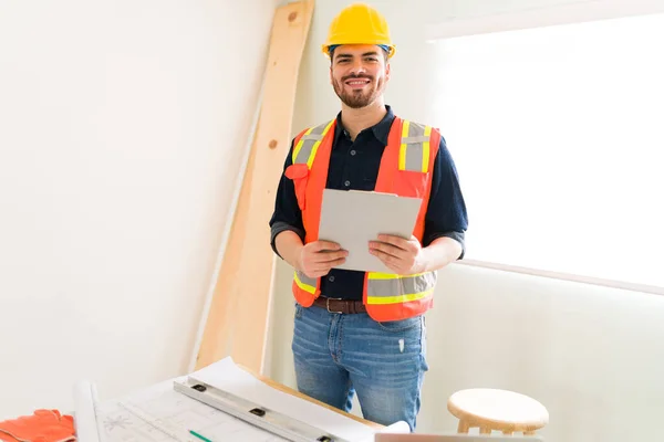 Feeling proud of my work. Smiling engineer wearing a yellow helmet and orange anti-reflective vest while getting ready to check on the construction site