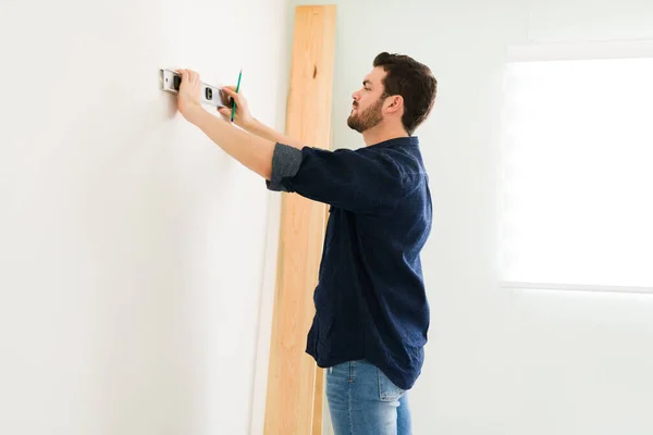 迷人的30多岁的男人用一个水平线上来检查新墙 勤杂工在家里做一些改进 — 图库照片