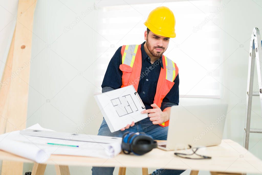 Do you approve of this construction plan? Professional male contractor showing the blueprints during an online video call on the construction site  