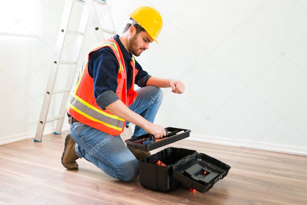 Young man or electrician with a safety helmet and orange vest using his toolbox to installing new electricity cables 