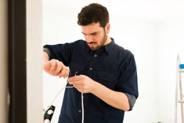 Odaklanmış bir adam ve ev sahibi evindeki elektrik sistemini tamir ediyor. Latin adam ışık düğmesini kontrol ediyor.