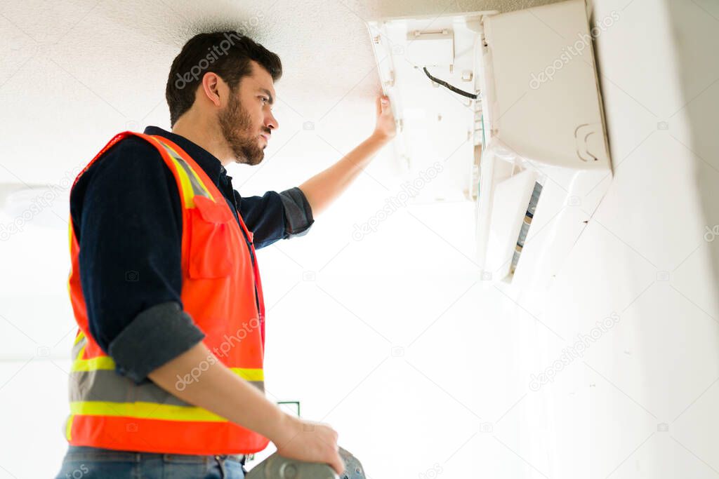 Side view of an attractive worker and electrician checking the air conditioner while giving maintenance 