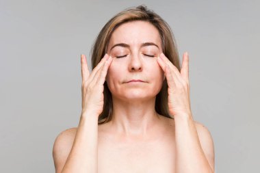 50 'li yaşlarda çekici bir kadının portresi göz kremi sürüyor ve cilt bakımını bitiriyor.