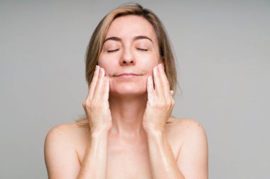 Cilt bakımını yaparken dinleniyorum. 50 'li yaşlarda güzel bir kadın yüzüne sabun sürüyor ve sağlıklı cildini yıkıyor.