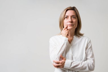 Olumlu şeyler düşünüyorum. 50 'li yaşlarındaki düşünceli çekici kadın yukarı bakıyor ve elleri çenesinde hayal gücünü kullanıyor.