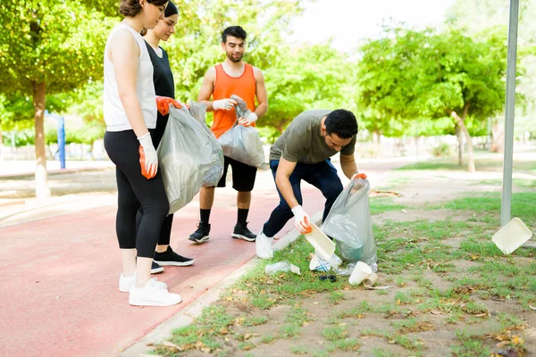 Young diverse friends with social responsibility collecting litter garbage on a trash bag while working out together at the park