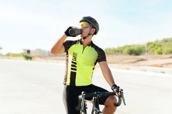 我非常口渴 瘦小的年轻运动员在自行车上休息和呼吸时 从瓶子里喝水 专业骑单车者水合物 — 图库照片
