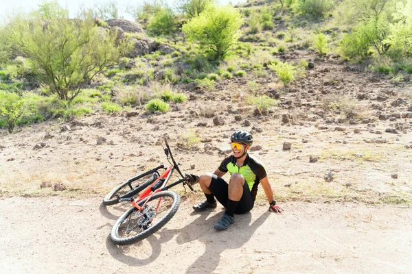 Happy young cyclist falling on his bike and laughing. Male cyclist suffering a little accident on his bicycle mountain outdoors