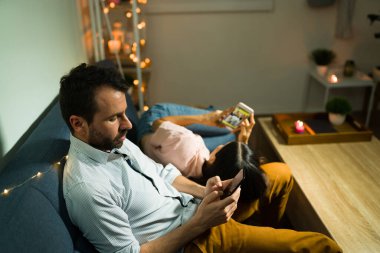 İşten sonra gevşeyeceğim. Yorgun genç bir çift, akıllı telefonlarına bakıp mesajlaşırken birlikte kanepede uzanıp dinleniyorlar.