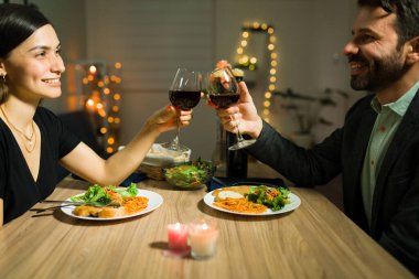 Çekici Latin çift evde evlilik yıldönümlerini kutlamak için süslü bir akşam yemeği yemeden önce şarapla kadeh kaldırıyor.